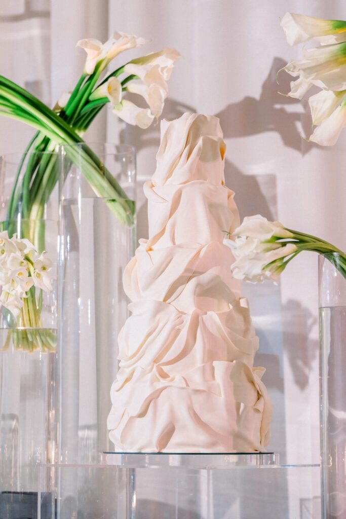 Sculptural wedding cake draped in folds of sugar like fabric, surrounded by calla lilies