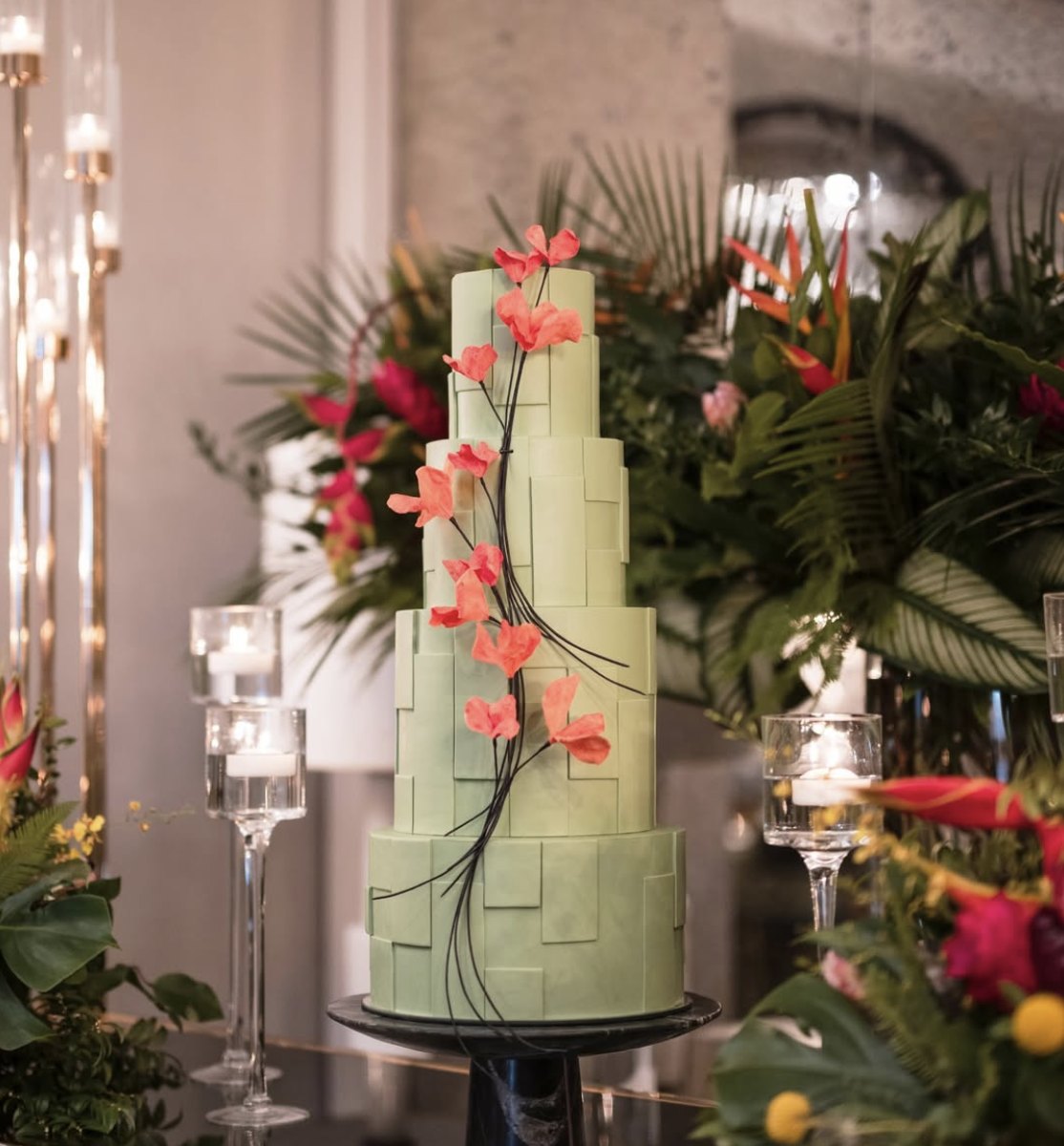 Pale green tiered cake with coral sugar flowers among tropical floral décor