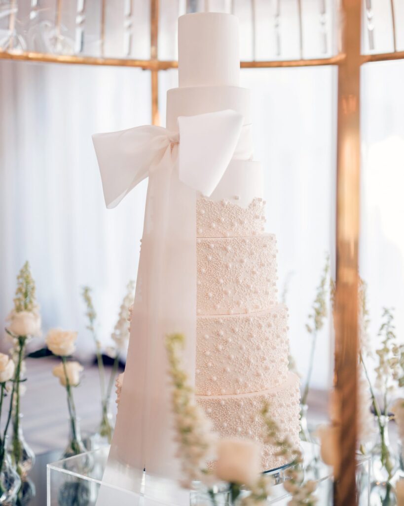 Tall wedding cake with sugar-pearl texture and a large white bow