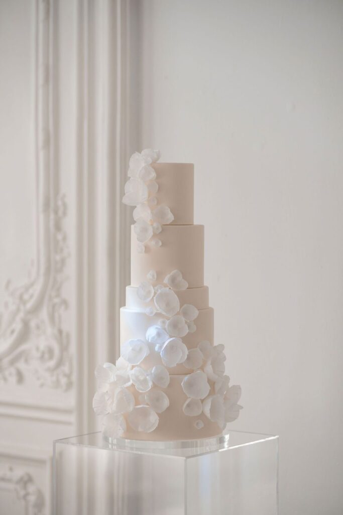 Five-tier blush wedding cake with a cascade of white wafer-paper flowers on a clear stand
