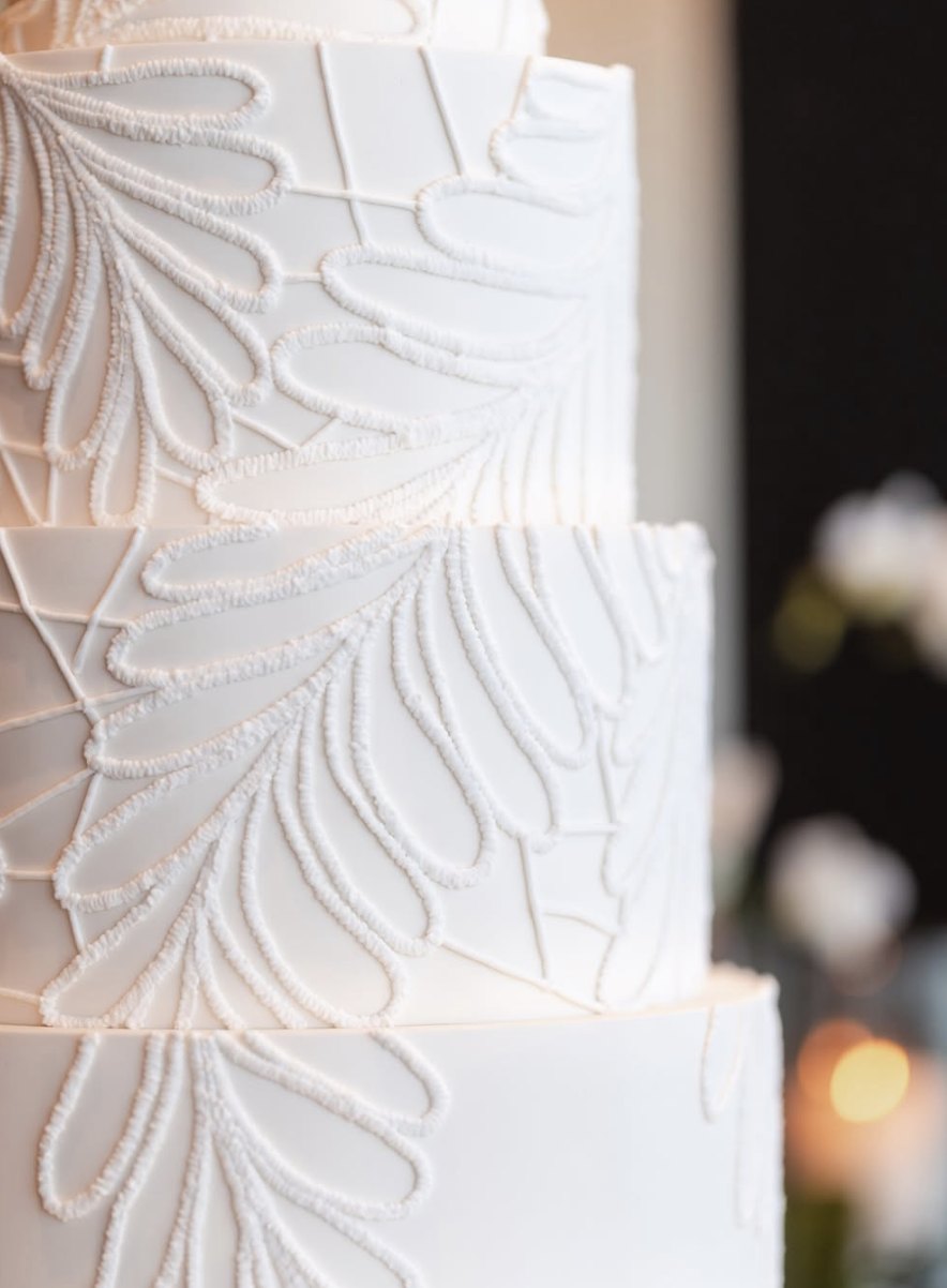 Close-up of hand-piped botanical lace on a white wedding cake