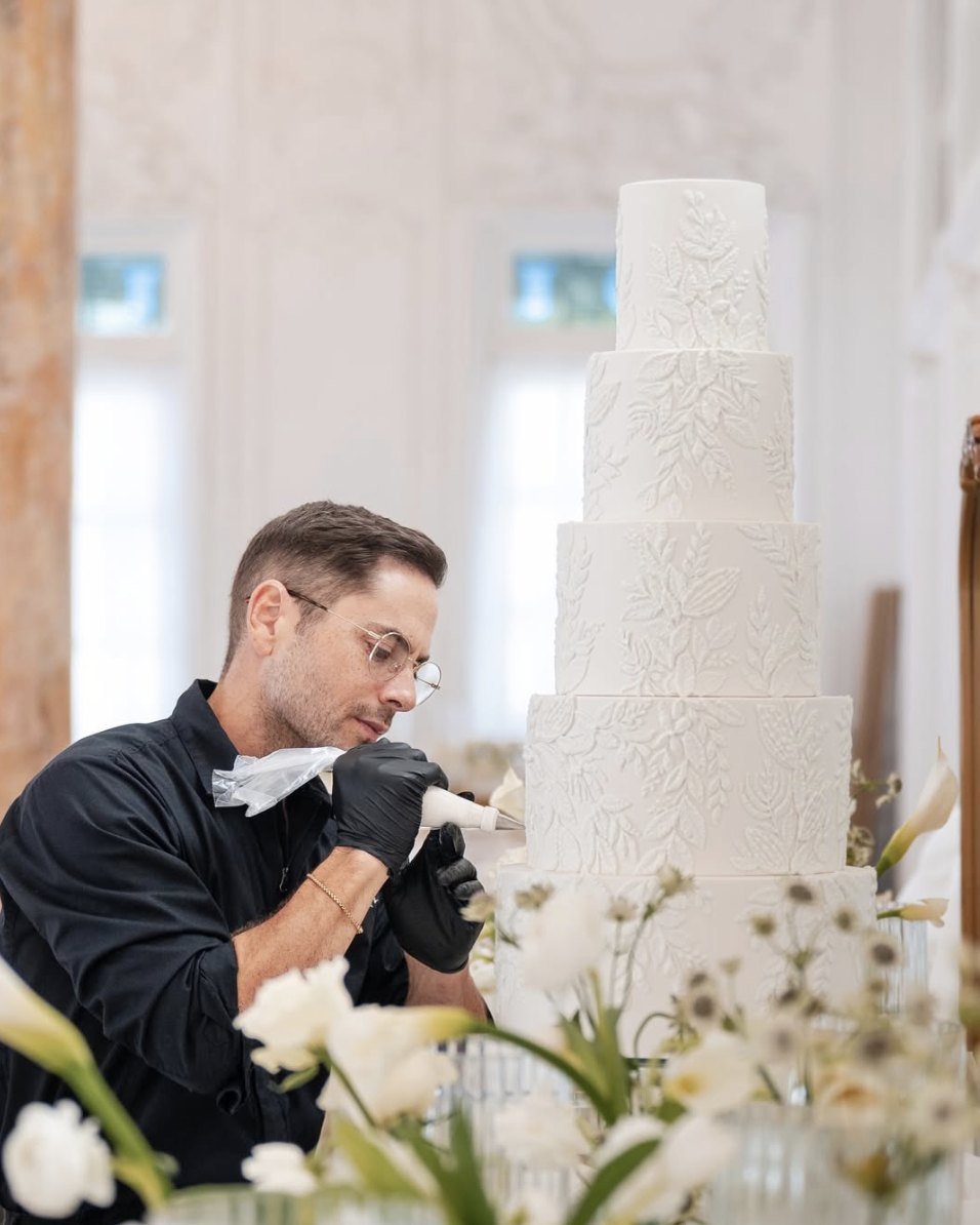 Cake designer Gabriel Díaz hand-piping details on a white tiered wedding cake